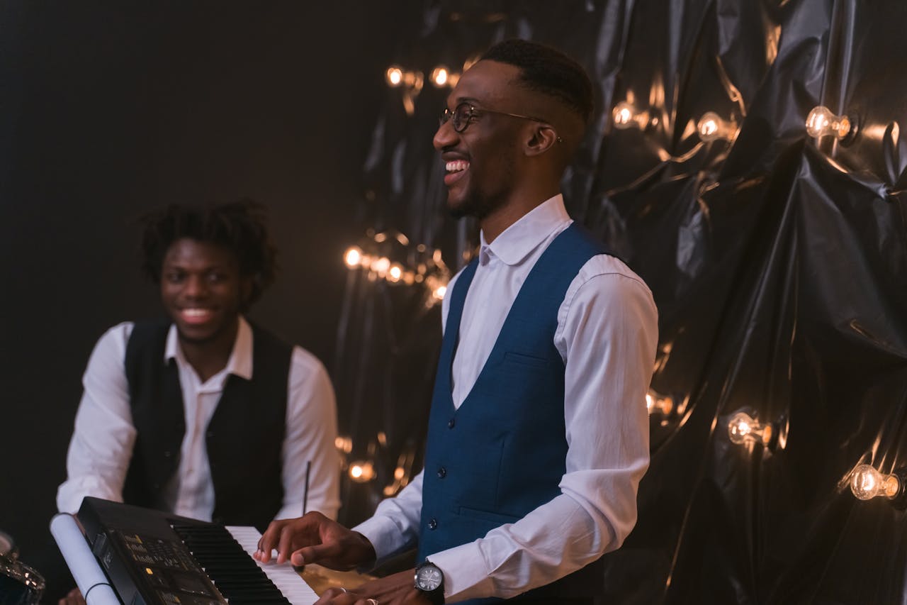 Two African American musicians joyfully performing, one playing the piano indoors.